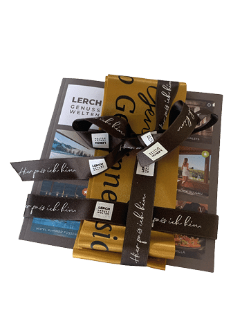 A neatly wrapped gift with a brown ribbon tied in a bow over a yellow and gray package featuring printed text and images. Beschreibung von KI generiert